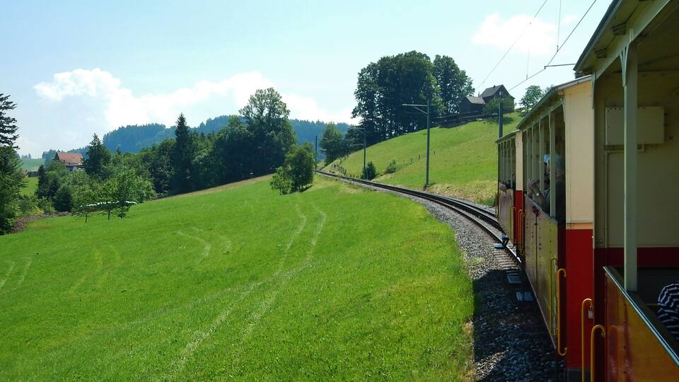 A train on a curved track through a green landscape with trees and hills in the background.