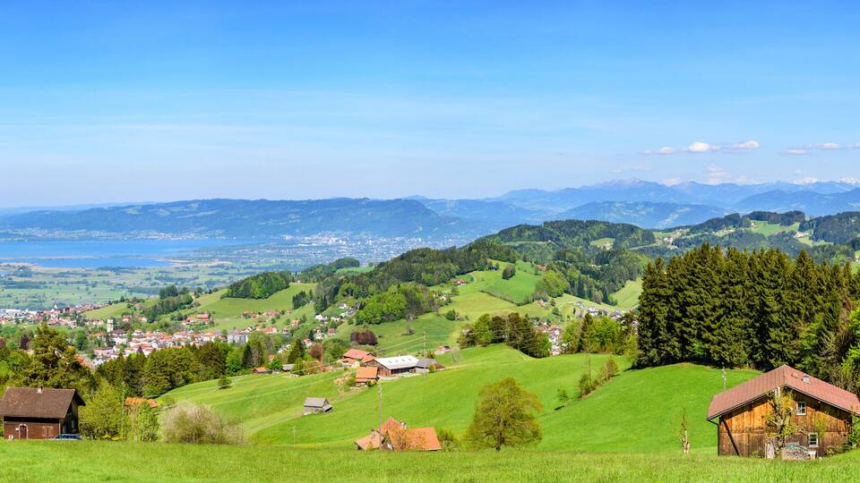 A mountainous landscape with a village, green fields, and a lake.