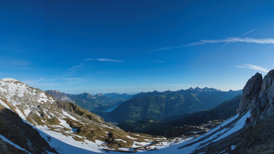 A mountain landscape with snow patches and a clear blue sky.