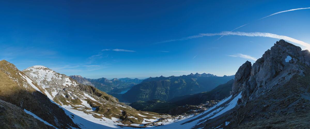 A mountain landscape with snow patches and a clear blue sky.