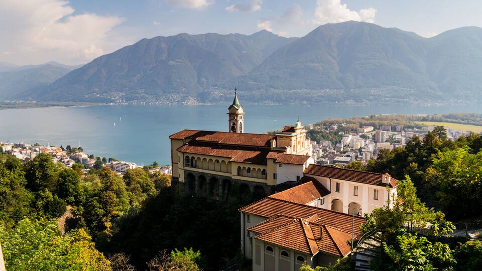 A coastal town with a prominent church, mountains in the background, and a lake.