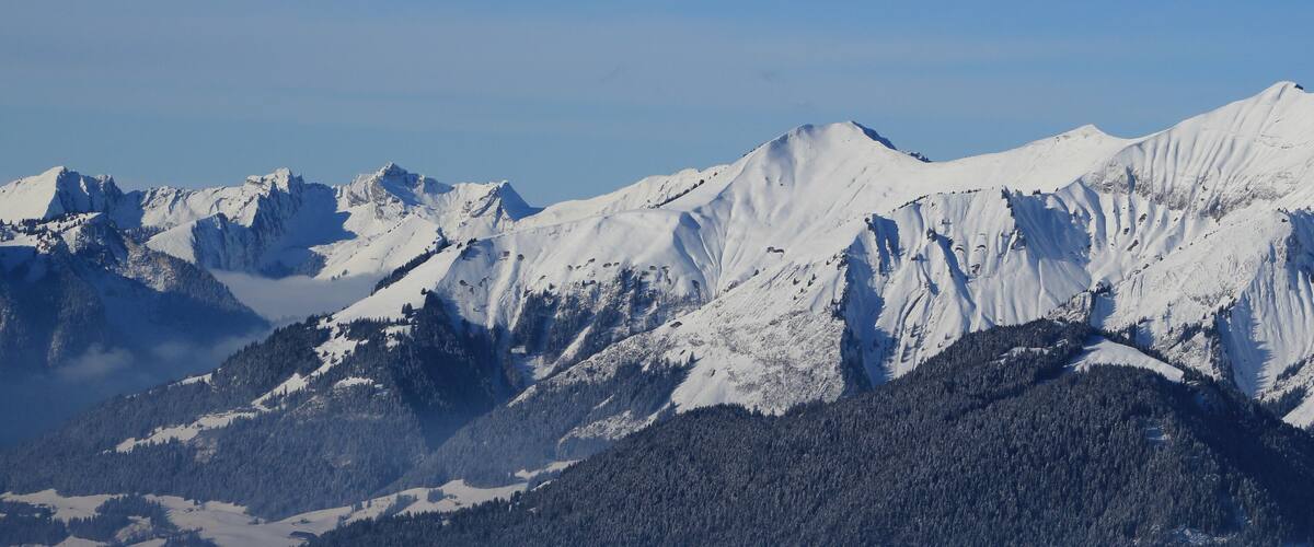 A snow-covered mountain range with sharp peaks and dense forests at the base.