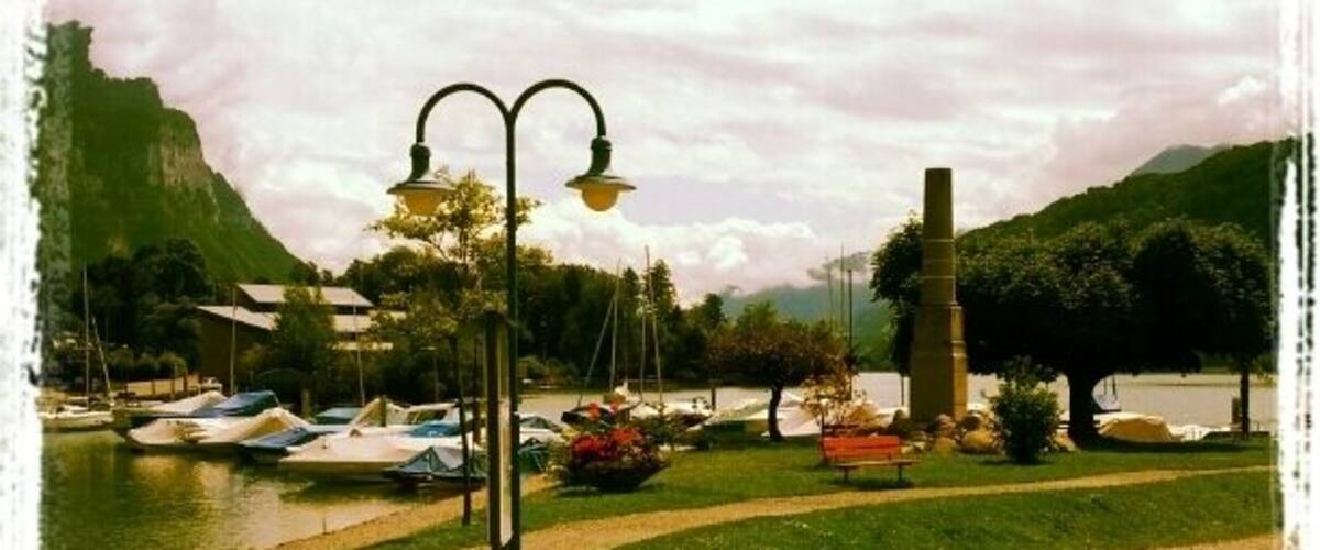 A lakeside park with boats, a lamp post, a bench, and a mountain in the background.