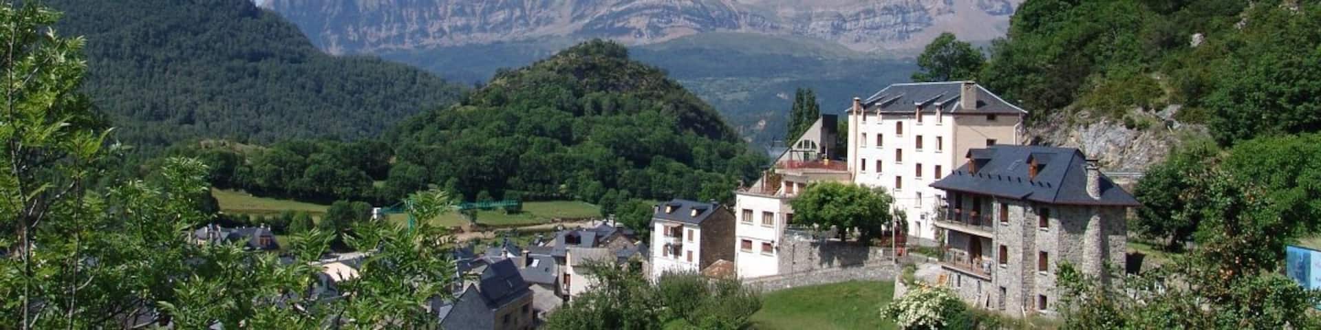 A mountainous landscape with a village, a prominent stone building, and lush greenery.