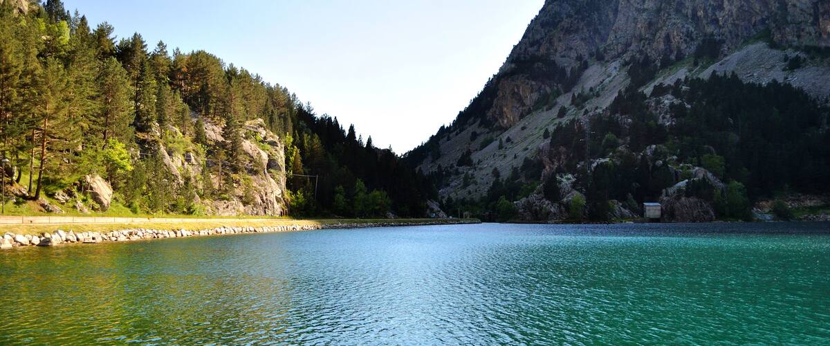 A calm lake surrounded by dense forests and rocky mountains.
