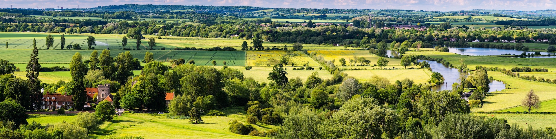 Un paisaje rural con campos, un río y una mansión.