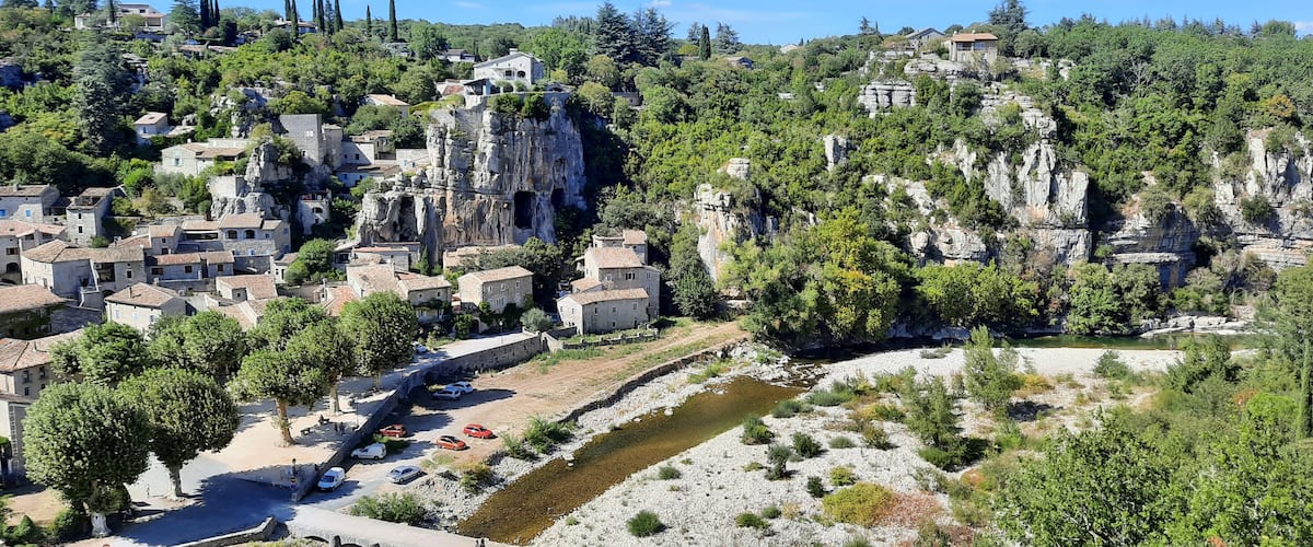 A village nestled in a valley with a river, surrounded by rocky cliffs and lush greenery.