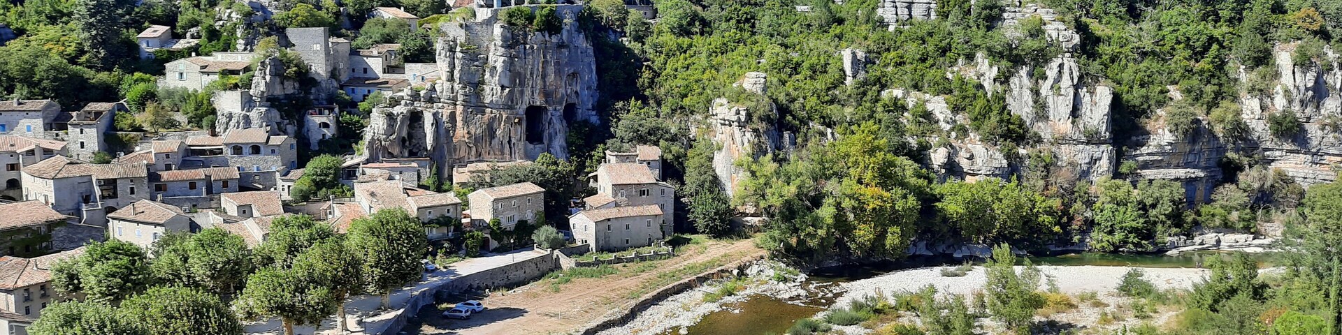 A village nestled in a valley with a river, surrounded by rocky cliffs and lush greenery.
