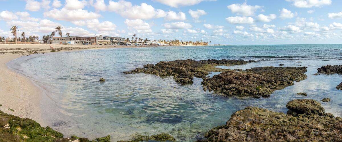 A beach with clear water, rocky outcrops, and palm trees.