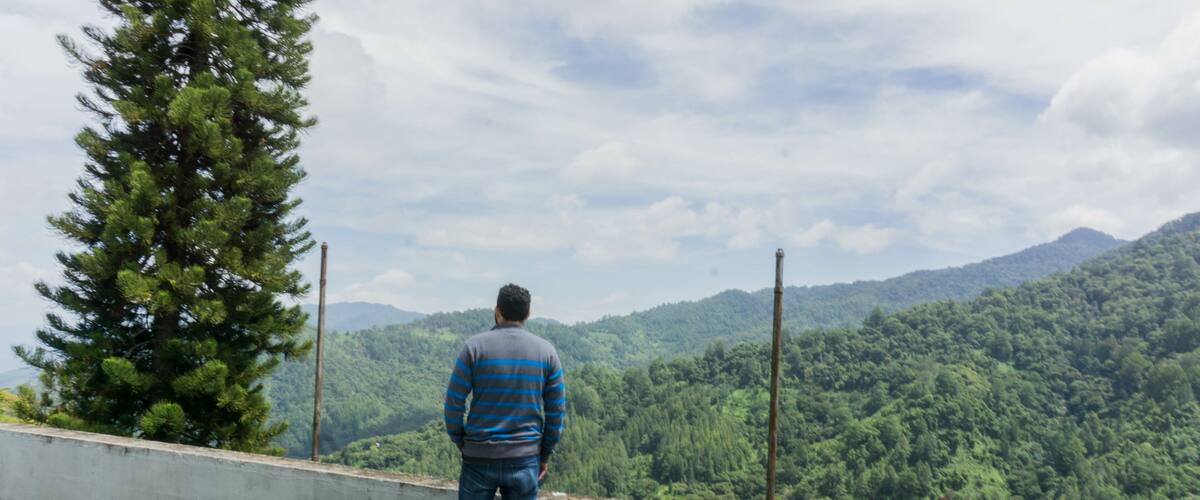 A man standing on a concrete ledge overlooking a forested mountain range.