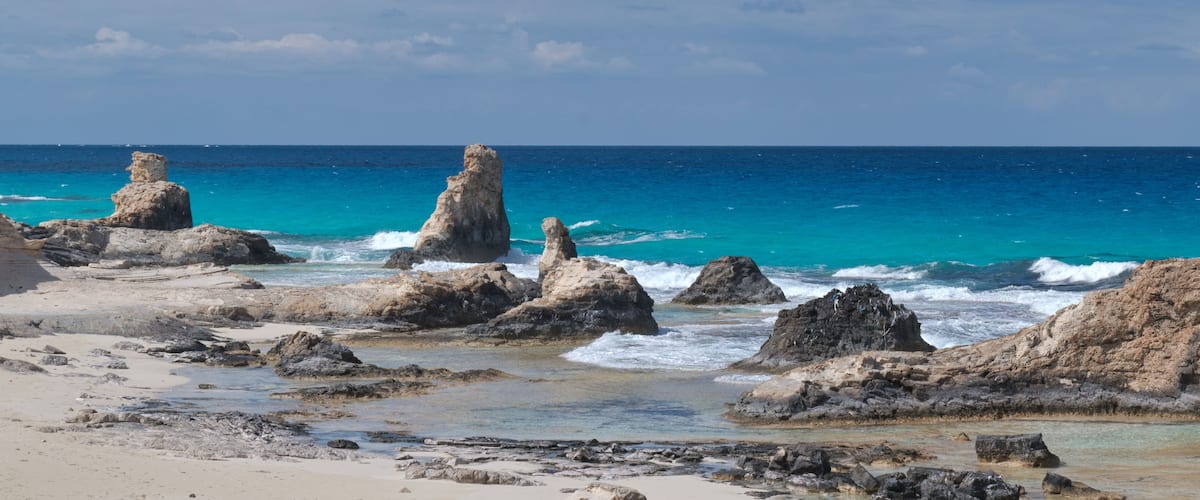 Litoral rochoso com águas turquesa cristalinas e céu limpo.