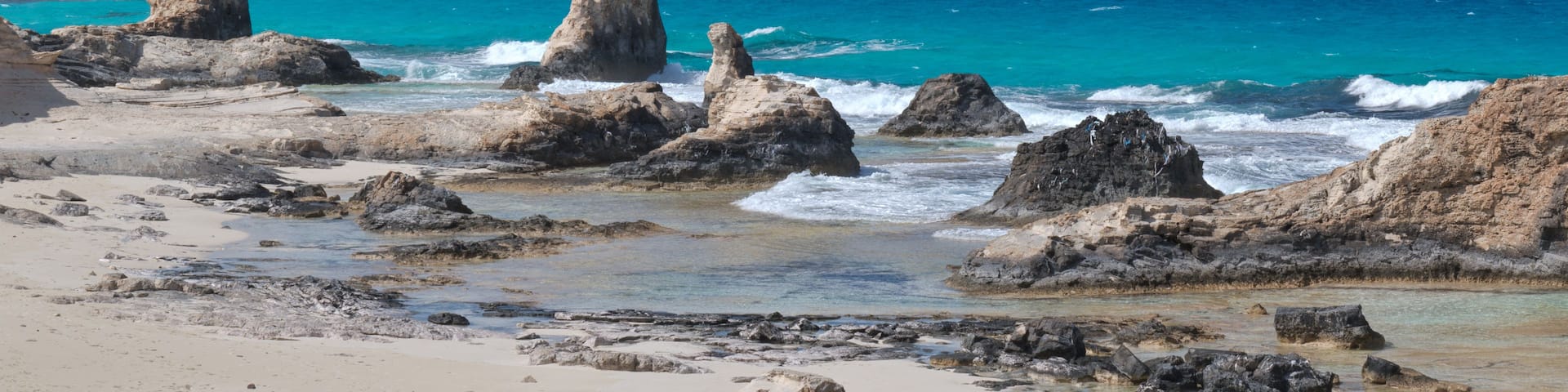 A rocky coastline with clear turquoise waters and a clear sky.