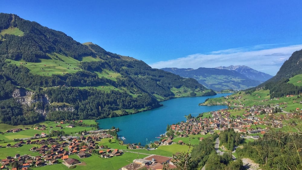 A mountainous landscape with a river, a small town, and green fields.