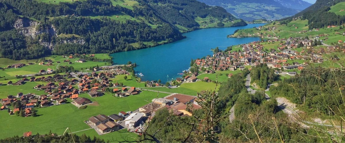 A mountainous landscape with a river, a small town, and green fields.