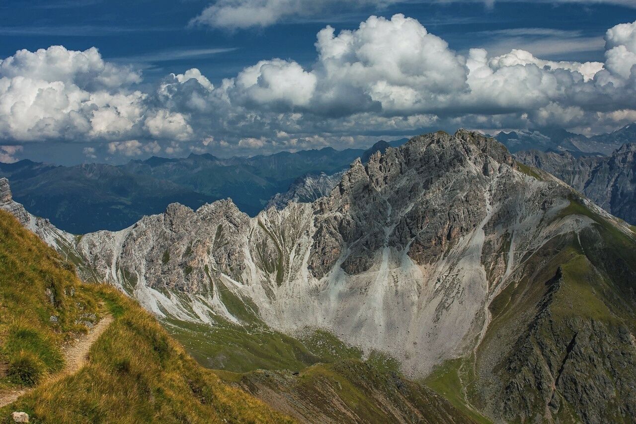 A rugged mountain range with a clear sky and a visible trail.