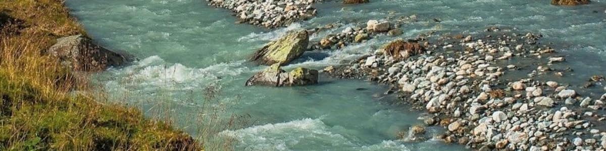 A river flowing through a mountainous landscape with rocky banks and a clear sky.