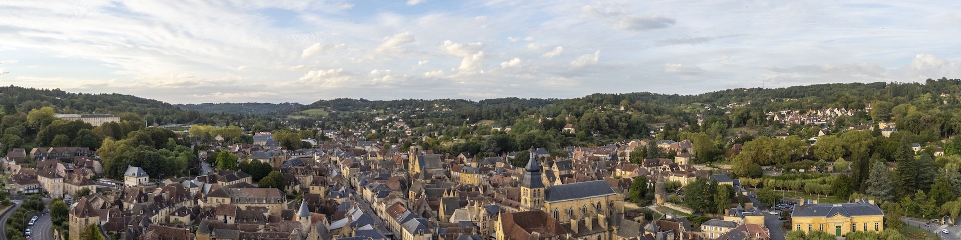 Aerial view of a tapestry of ochre rooftops and golden stone buildings nestled amidst verdant trees, overlooked by the imposing church tower, Le Buisson-de-Cadouin, Nouvelle-Aquitaine, France.