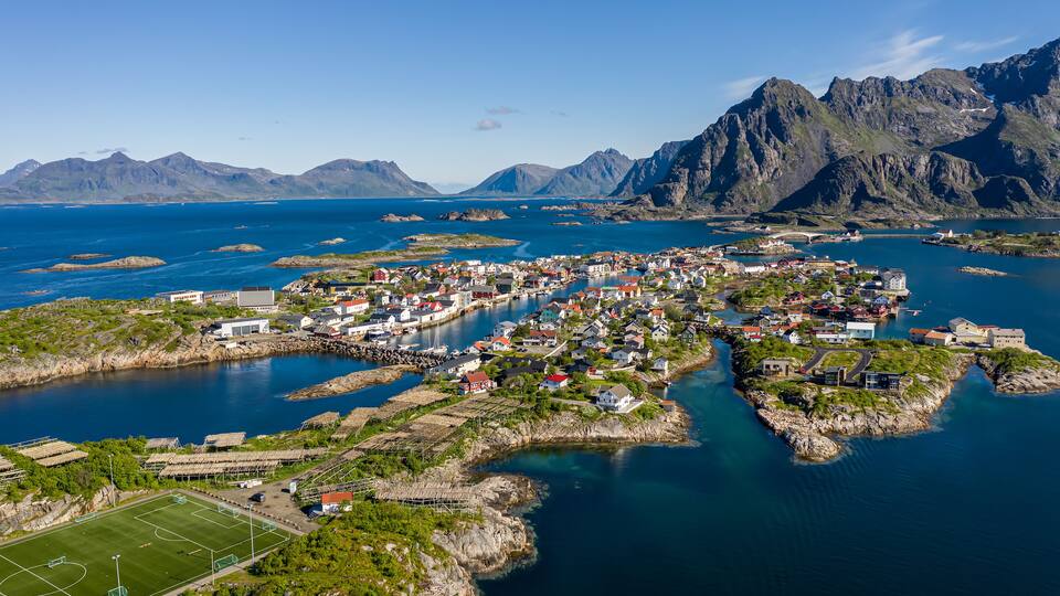 A coastal town with a harbor, mountains in the background, and a sports field.