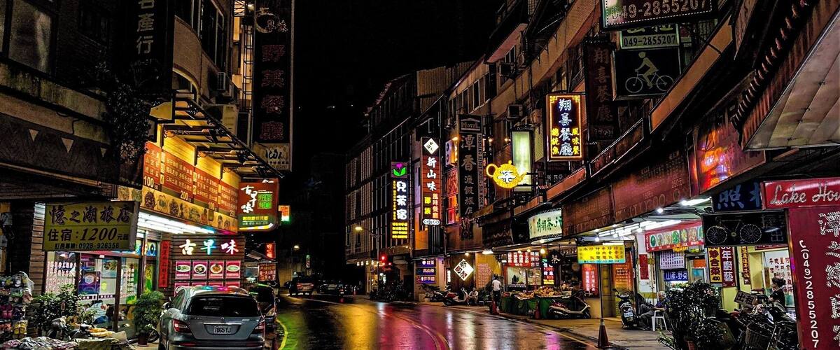 A wet street at night with neon signs and storefronts.