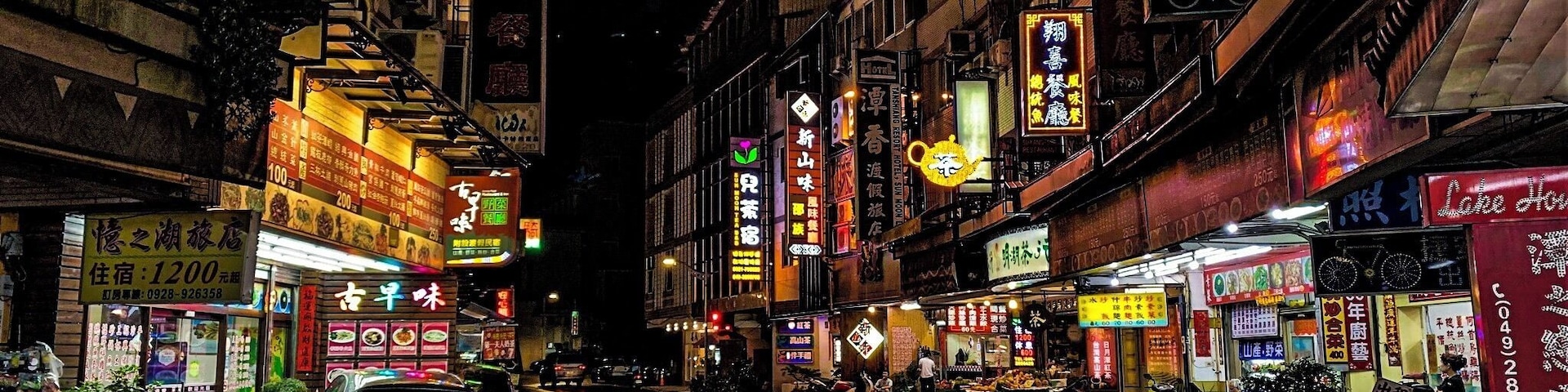 A wet street at night with neon signs and storefronts.