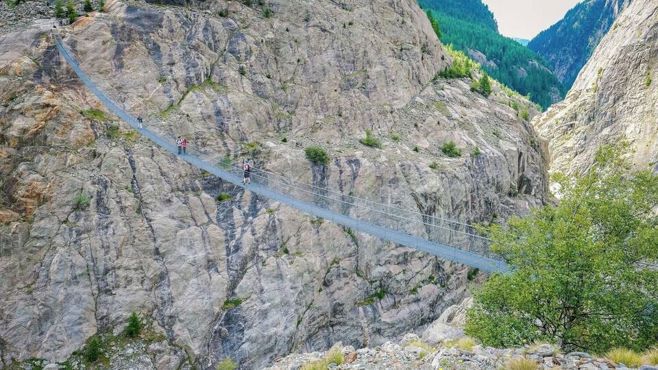 A suspension bridge in a mountainous area with rocky cliffs and greenery.