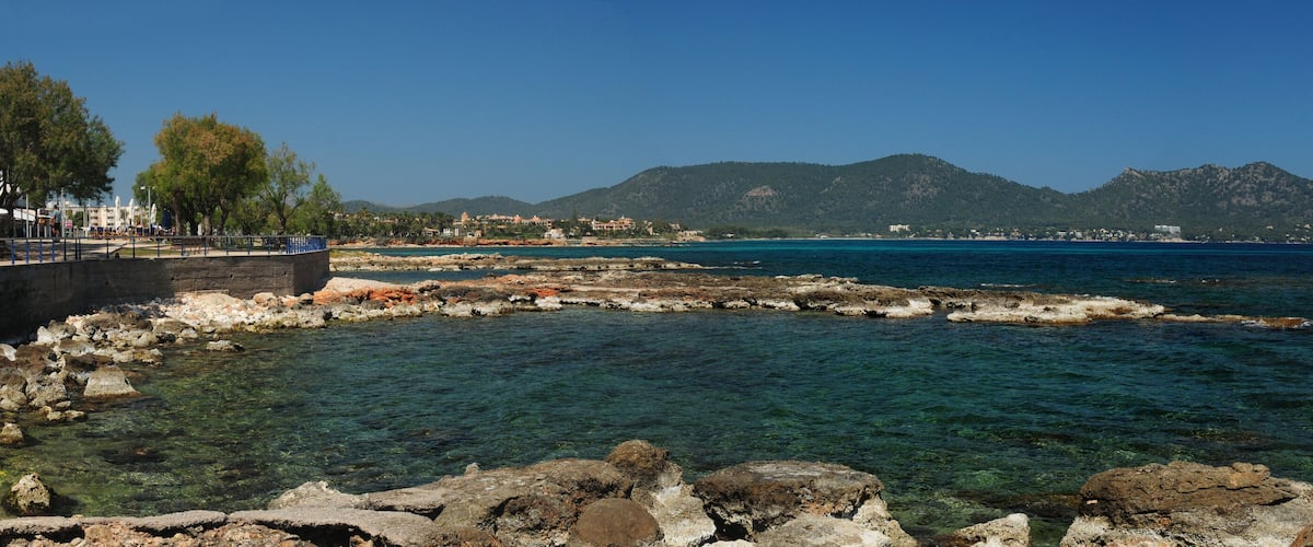 A coastal landscape with clear waters, rocky shorelines, and distant mountains.