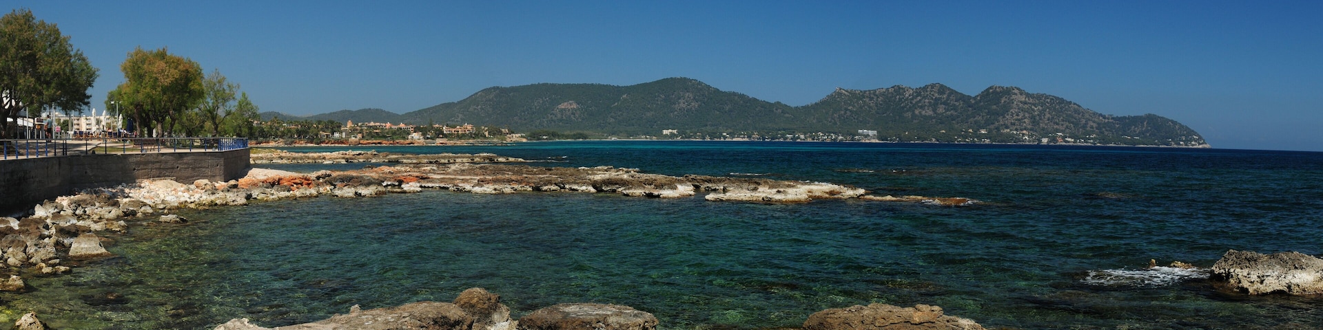A coastal landscape with clear waters, rocky shorelines, and distant mountains.