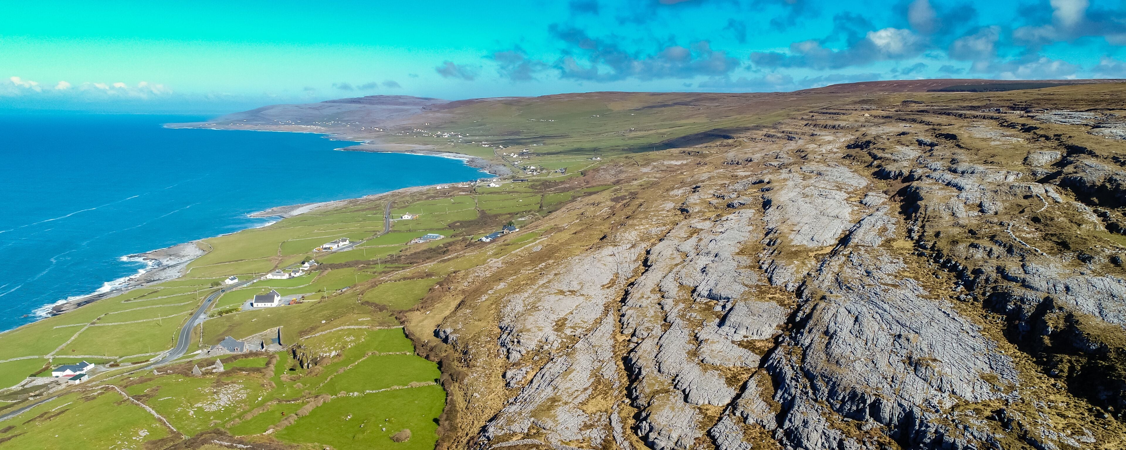A coastal landscape with rocky cliffs, a winding road, and scattered houses.