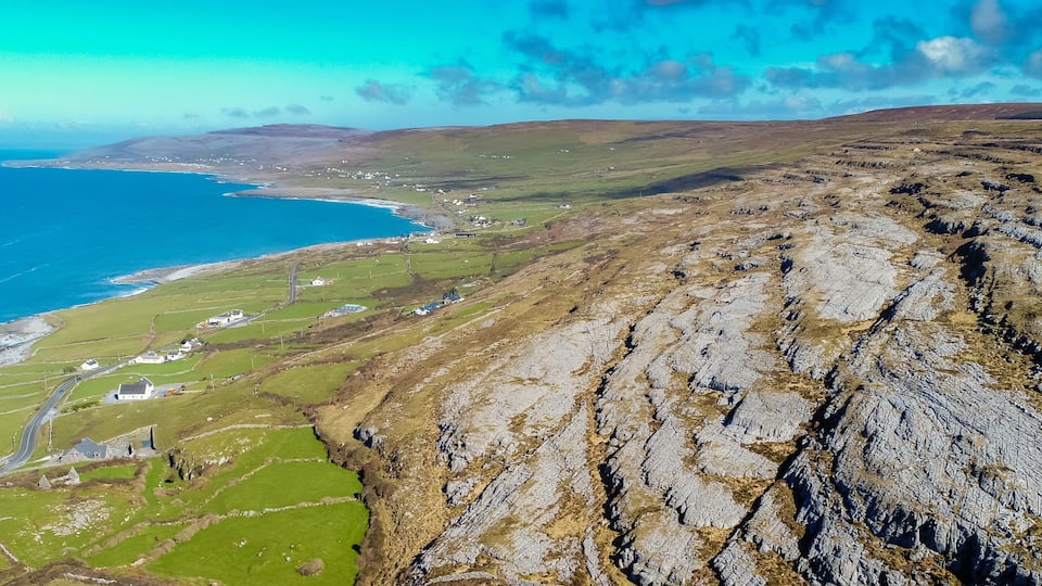 A coastal landscape with rocky cliffs, a winding road, and scattered houses.