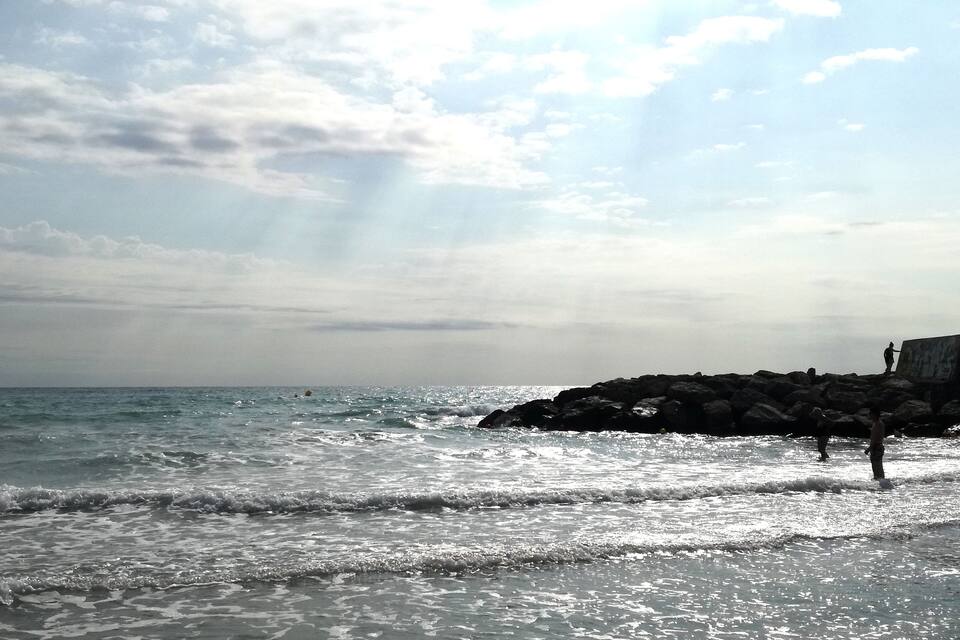 A rocky shoreline with waves crashing onto the beach and a person standing on the rocks.