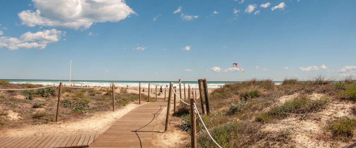 A wooden boardwalk leading to a beach with a kite flying in the sky.