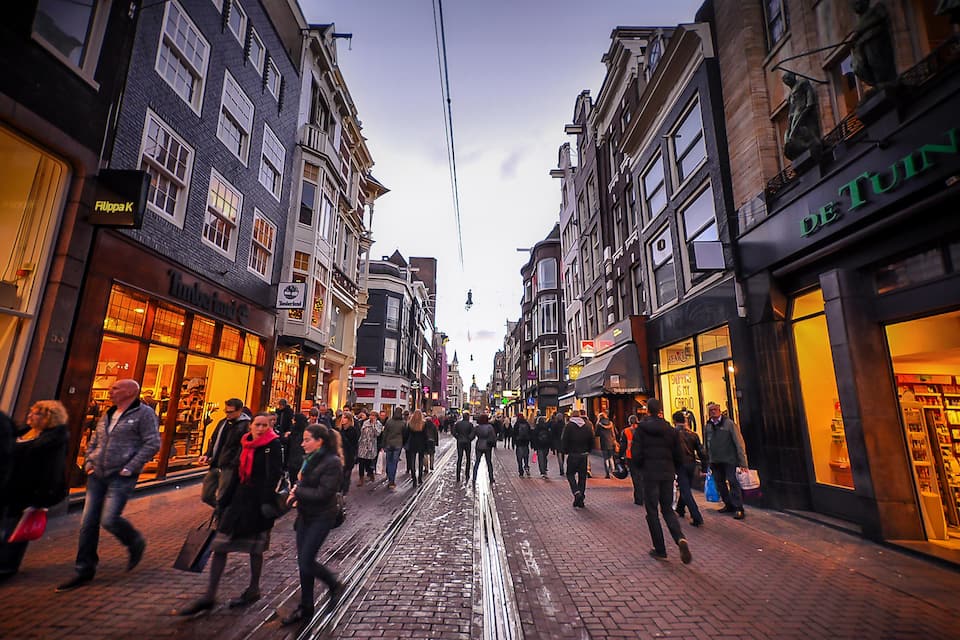 Une rue animée, où l’on voit des gens se promener, des boutiques de chaque côté et une voie ferrée pour tramway au milieu.
