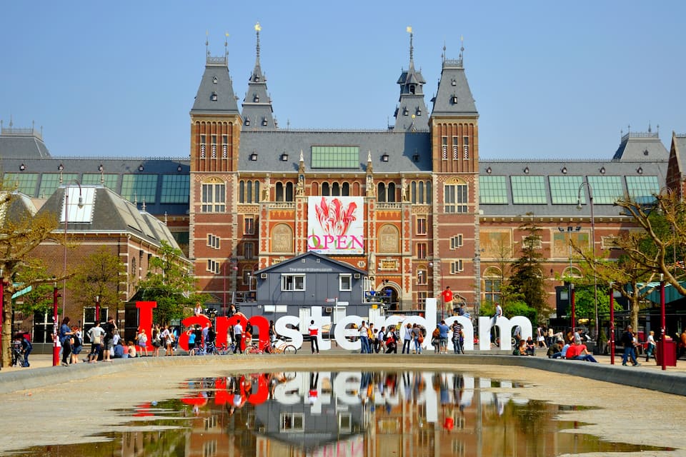 A historic building with a large 'Open' sign, a moat, and people around.