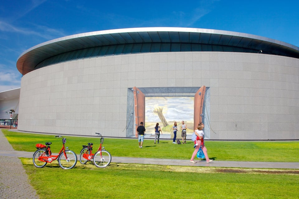 A modern circular building with a large mural of people on its facade.