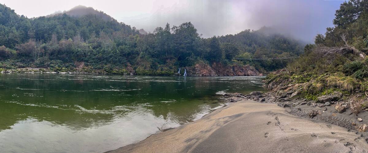 A river with clear water, surrounded by dense forest and rocky terrain.