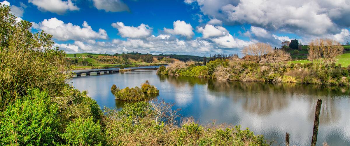 A river with a bridge, surrounded by greenery and hills.