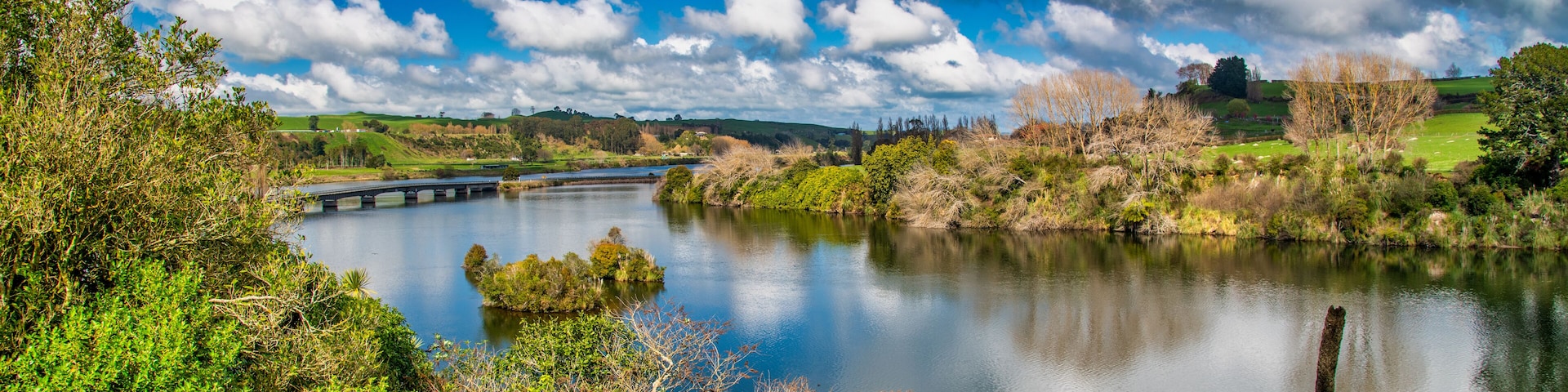 A river with a bridge, surrounded by greenery and hills.