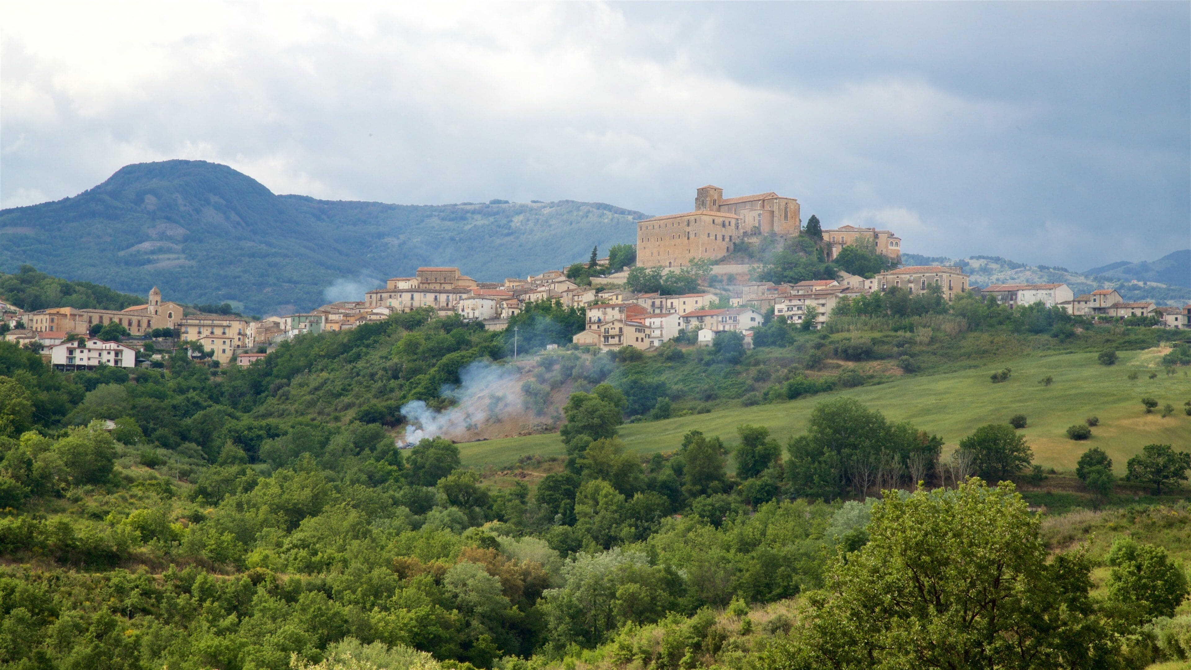 A historic town with a prominent castle on a hill, surrounded by lush greenery and rolling hills.