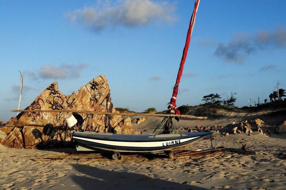 En sejlbåd ved navn "LUJANE" på en sandstrand med klippeformationer i baggrunden.