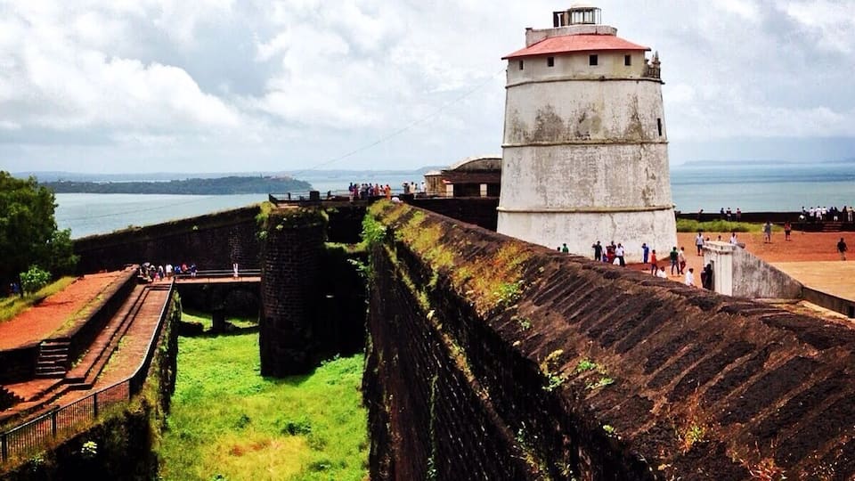 A coastal fort with a lighthouse, surrounded by a fortified wall and a grassy area.