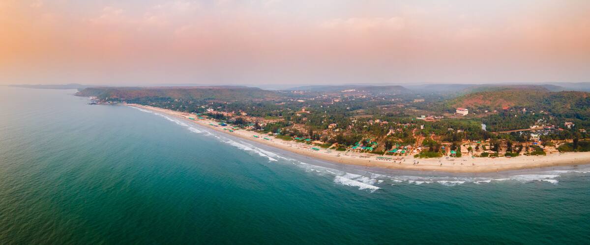 An aerial view of a coastal town with a beach, houses, and hills in the background.