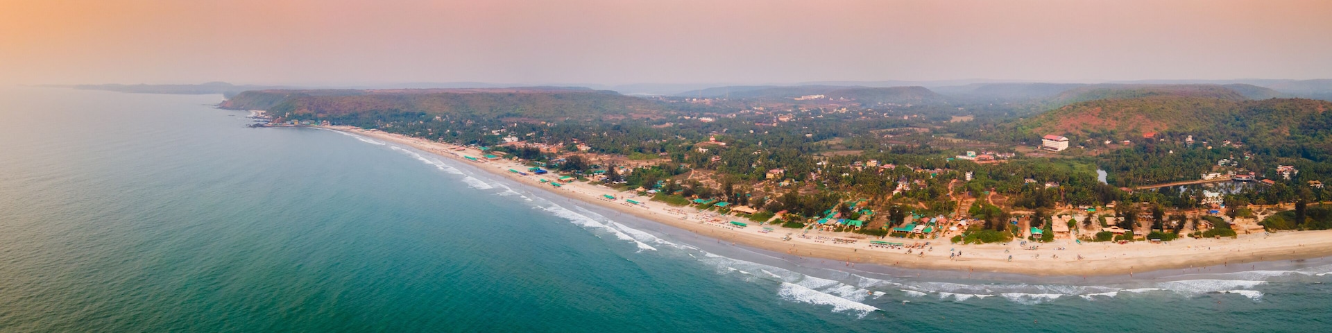 An aerial view of a coastal town with a beach, houses, and hills in the background.