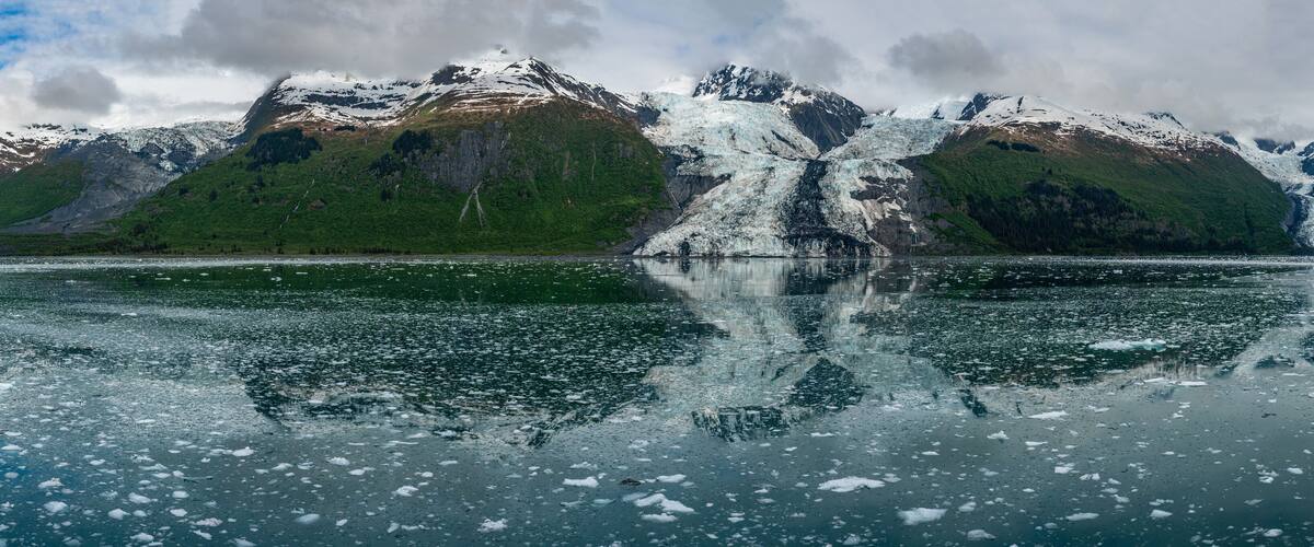 A glacier with a waterfall, surrounded by mountains and a lake.