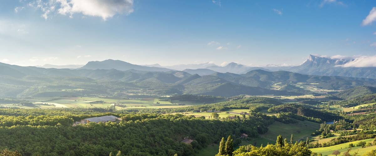 A mountainous landscape with rolling hills, a lake, and scattered buildings.