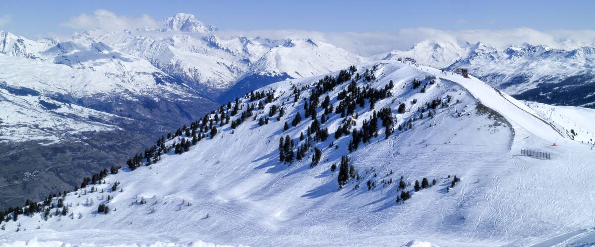 A snow-covered mountain slope with a ski trail and a clear blue sky.