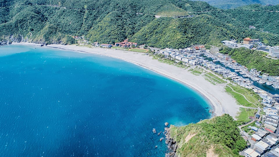 A coastal area with a beach, a marina, and a mountainous backdrop.