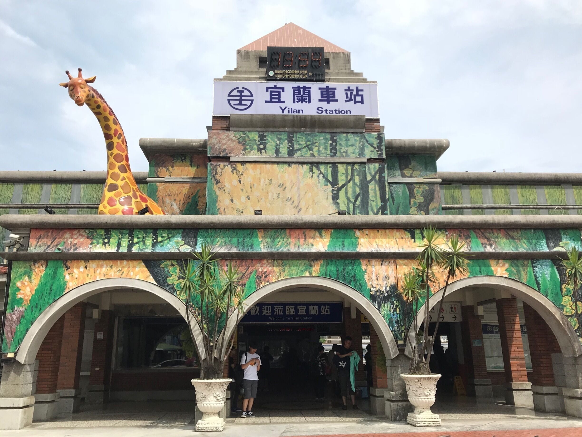 A station with a giraffe sculpture, a sign reading "Yilan Station," and a mural of trees.