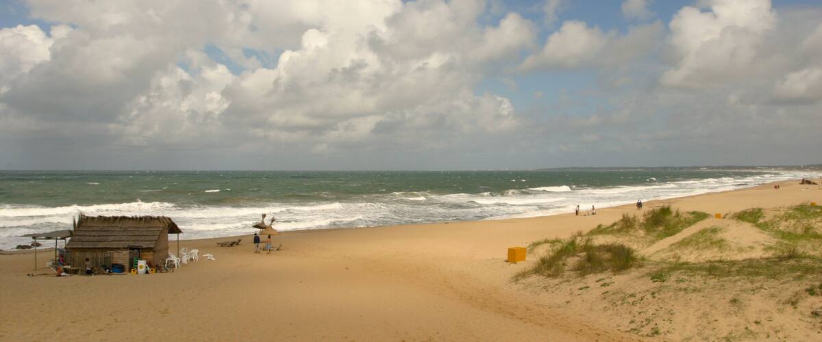 A beach with a hut, people, and waves.