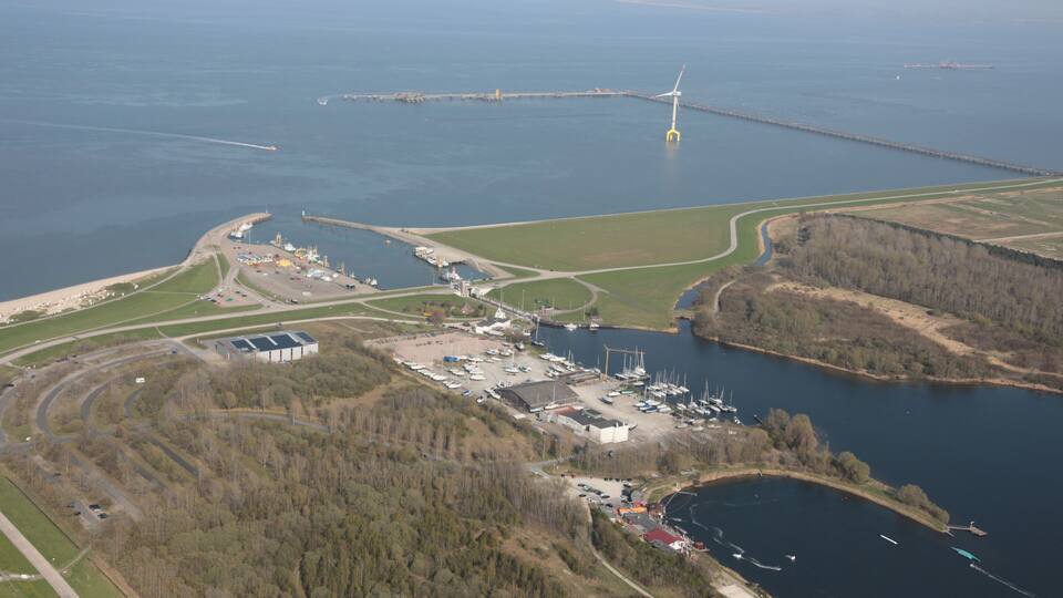 An aerial view of a coastal area with a marina, a wind turbine, and a large body of water.