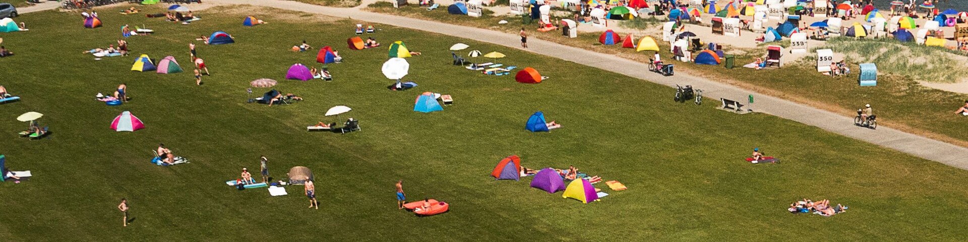 Praia cheia com várias barracas coloridas e pessoas aproveitando o mar.
